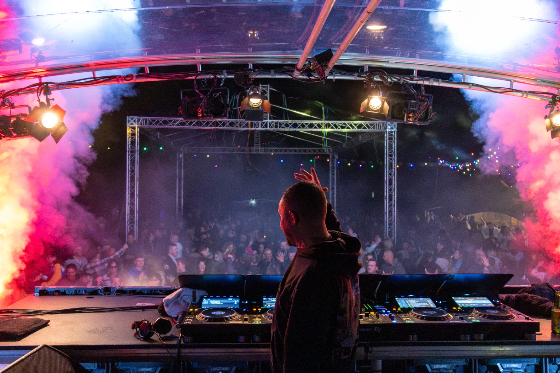 DJ achter draaitafels met juichend publiek in roze rook en spotlights
